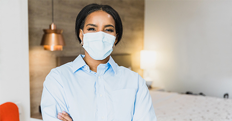 Woman wearing face mask stands in hotel room