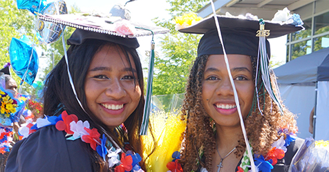 Two graduates smile at Commencement.