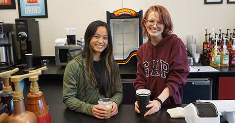 Two students smile behind the cafe's counter.